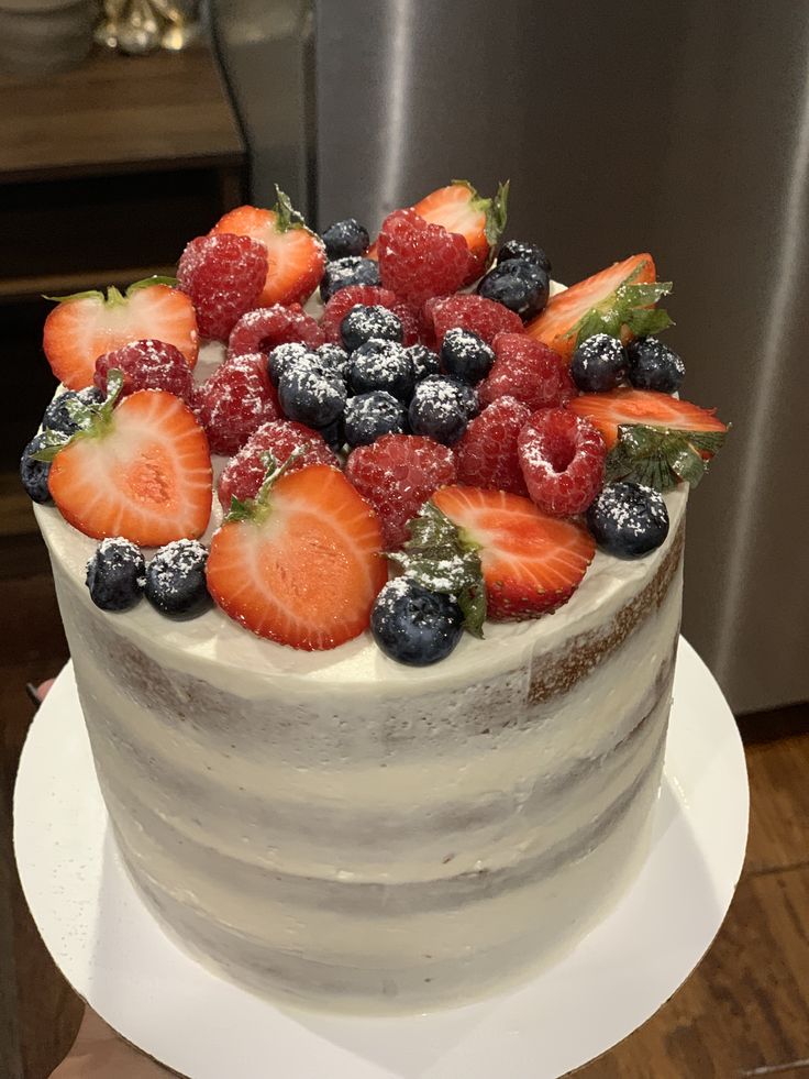 a white cake with berries and powdered sugar on top is sitting on a table