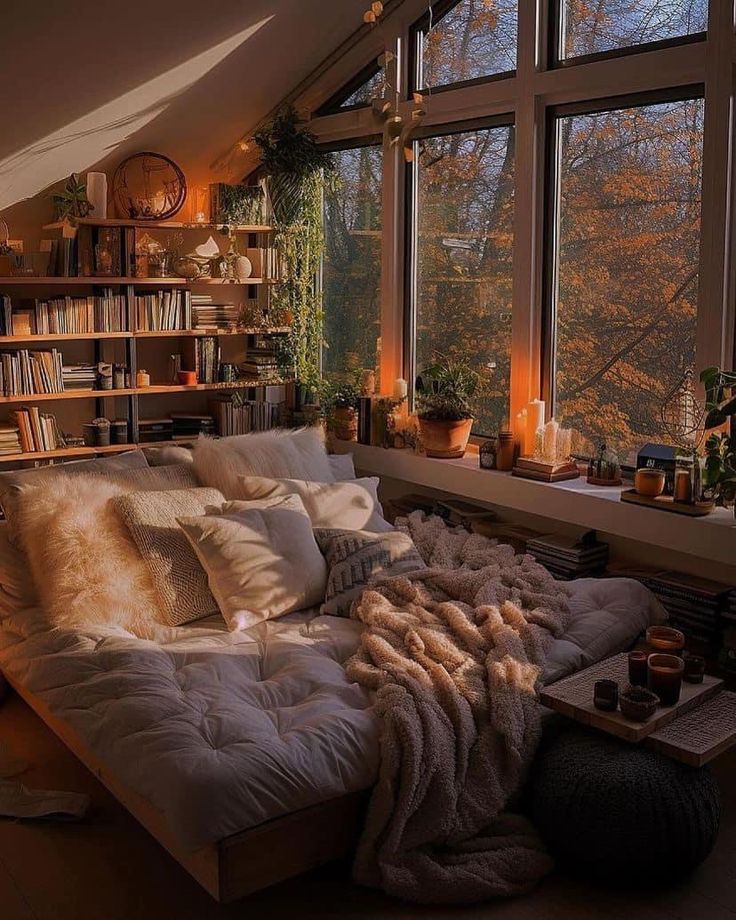 a bed sitting in the middle of a living room next to a window filled with books