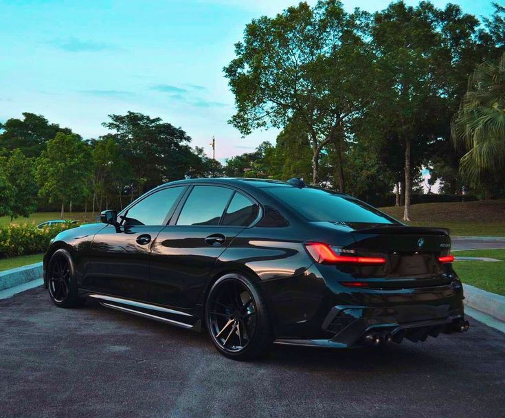 a black car parked in a parking lot next to some trees and bushes on the side of the road