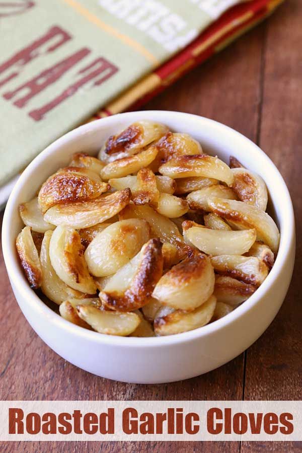 roasted garlic cloves in a white bowl on a wooden table next to a book