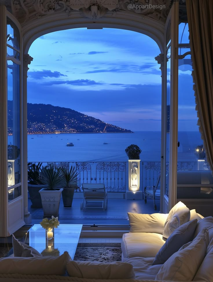 a living room filled with furniture next to a large window overlooking the ocean at night