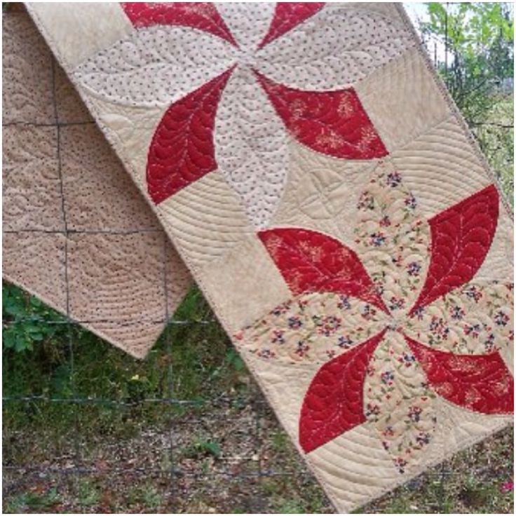 two quilts are hanging on a fence in the grass and one has a red flower