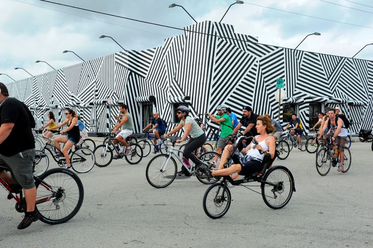 a group of people riding bikes down a street in front of a building with black and white stripes on it