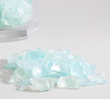 some blue and white rocks on a table next to a glass vase with water in it