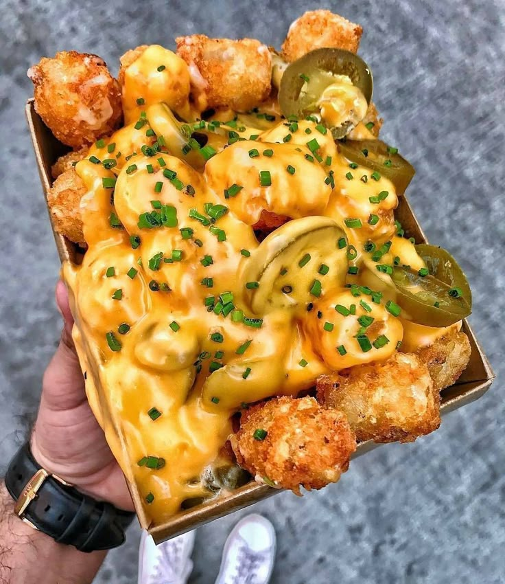 a person holding up a box filled with macaroni and cheese covered in sauce