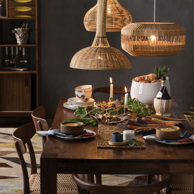 a dining room table is set with food and candles in the center, surrounded by wicker hanging lights