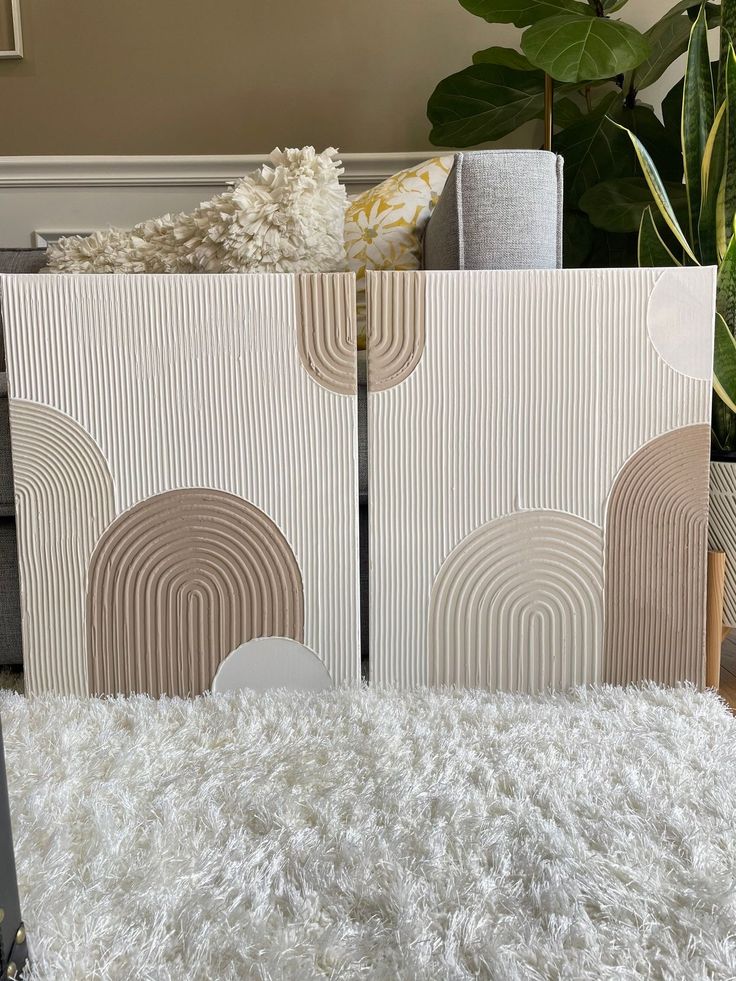 a living room with a white rug and two pieces of art on the wall next to each other