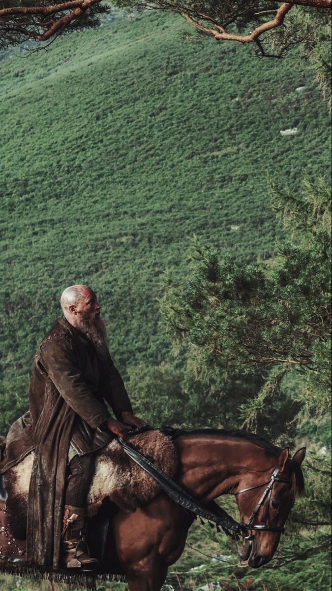 an old man riding on the back of a brown horse next to a lush green hillside