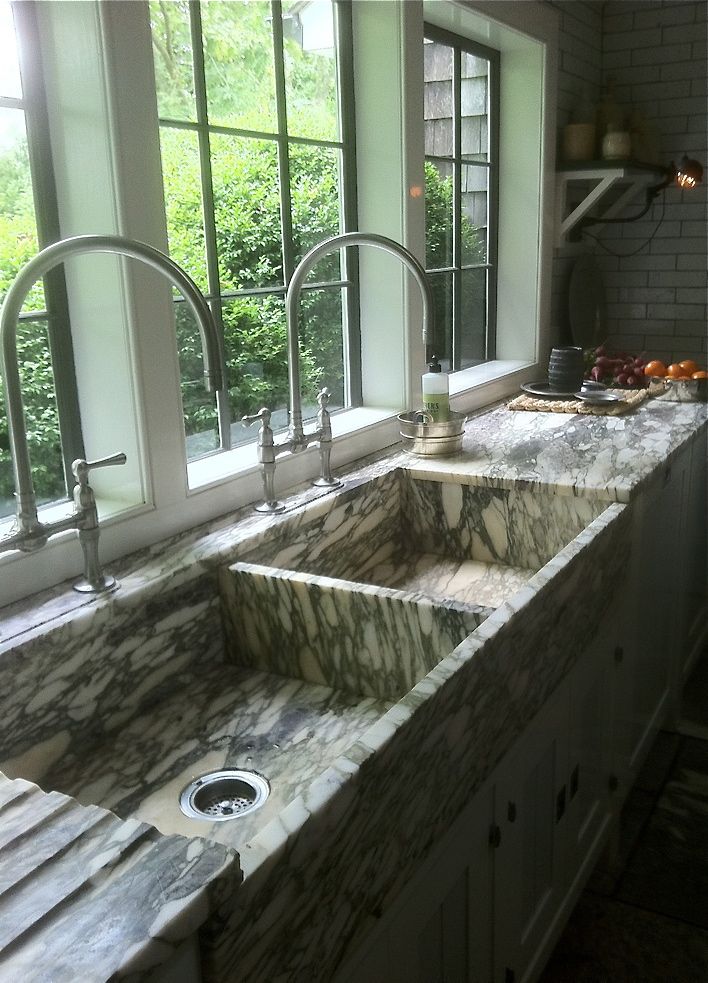 a kitchen with marble counter tops and double sinks in front of large windows overlooking trees