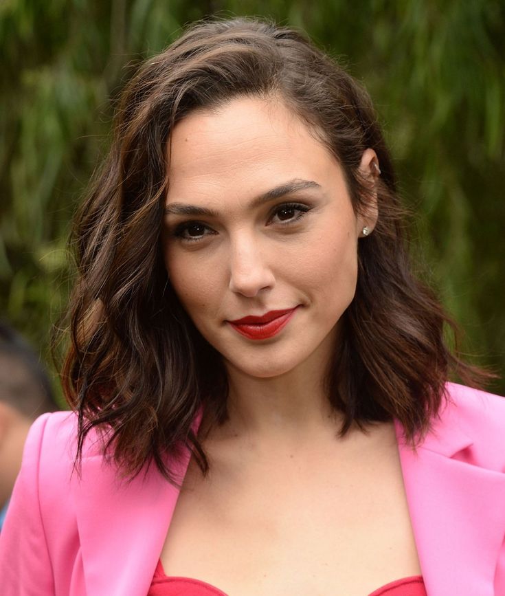 a close up of a person wearing a pink suit and red lipstick with trees in the background