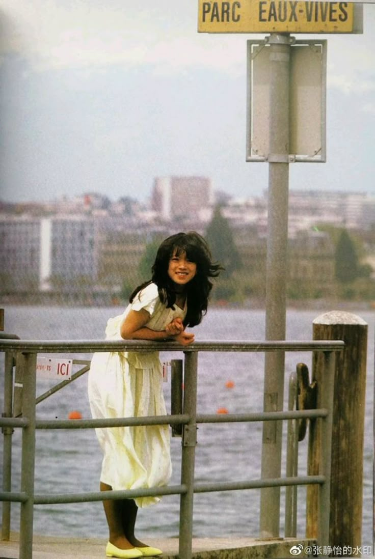 a woman in white dress standing on pier next to water and street sign that reads paris eaux - vies