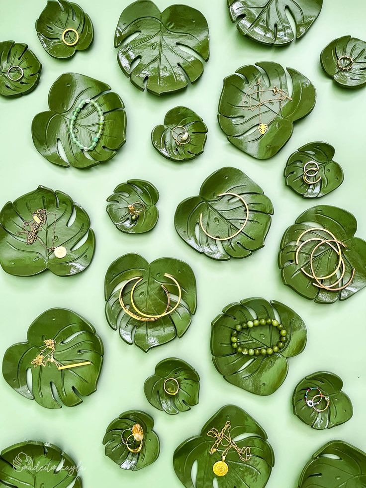 many green leaf shaped objects are arranged on a light green surface with gold rings and beads