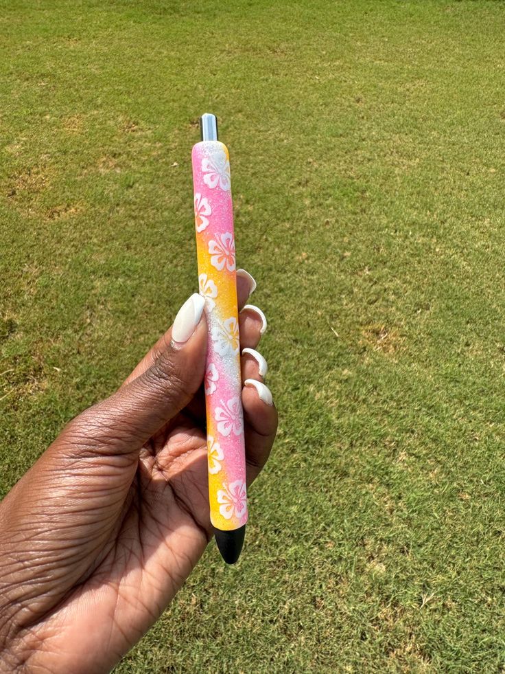 a hand holding a pink and yellow pen on top of a green grass covered field