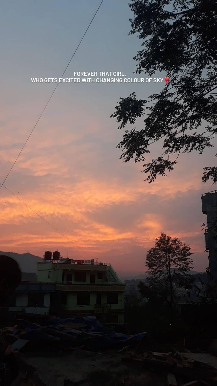 the sun is setting over some houses and trees in front of a building with power lines above it