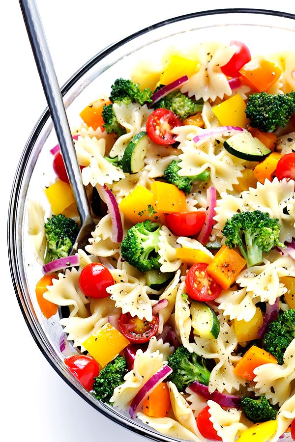 a pasta salad with broccoli, carrots and red onions in a glass bowl