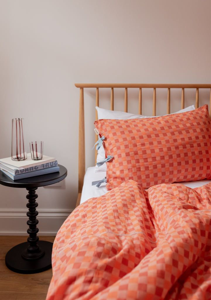 an orange and white checkered comforter on a bed next to a night stand