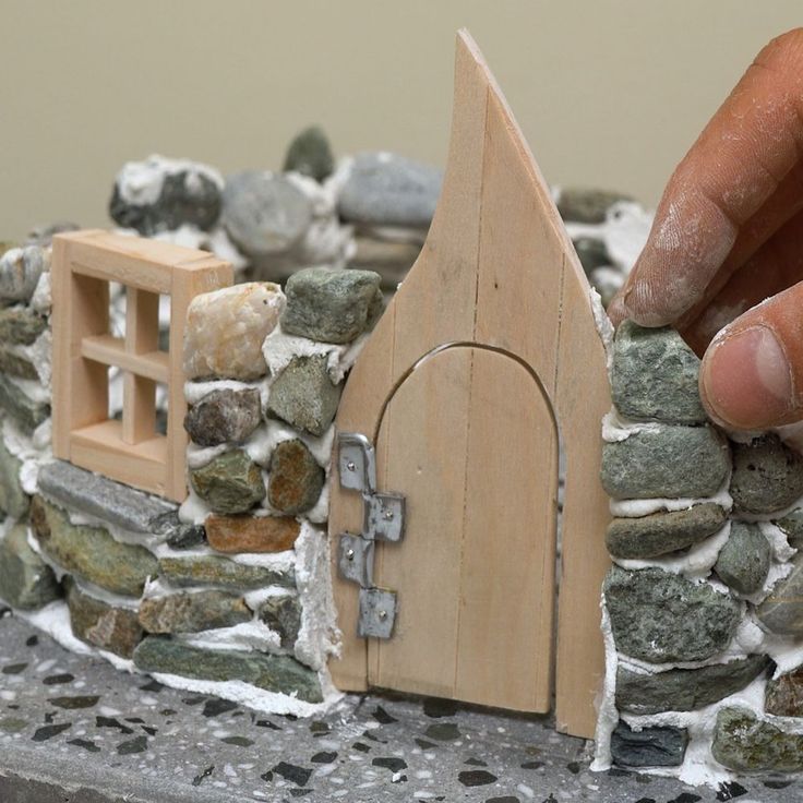 a hand is touching the door to a small house made out of rocks and wood