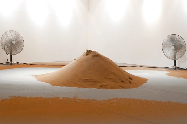 two fans sitting on top of a floor next to a pile of sand in front of a white wall