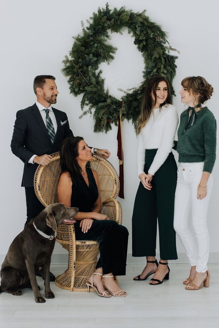 three people and a dog sitting in front of a christmas wreath