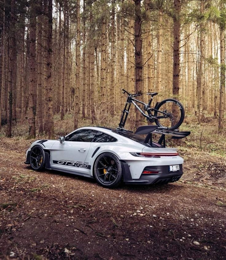 a white sports car parked in the woods with a bike on it's roof