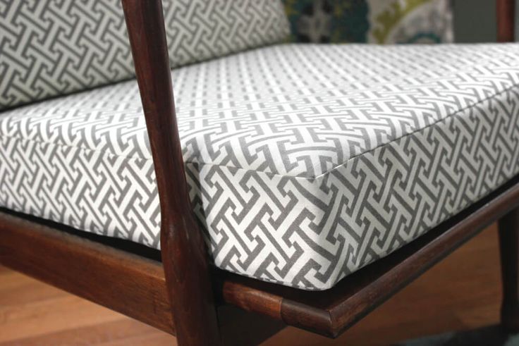 a close up of a wooden chair with a white and black patterned seat cover on it