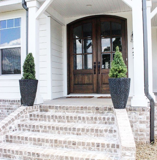 a white house with two large planters on the front steps and a brown door