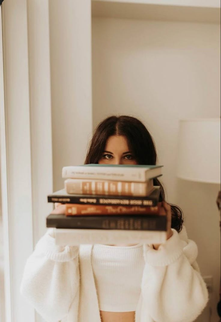 a woman is holding several books on her shoulders and looking at the camera while standing in front of a mirror