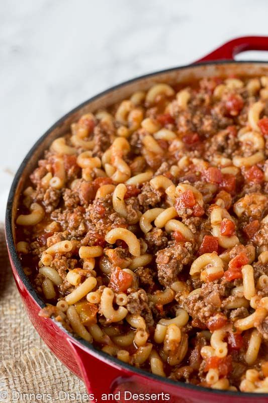 a large red pot filled with pasta and ground beef on top of a wooden table