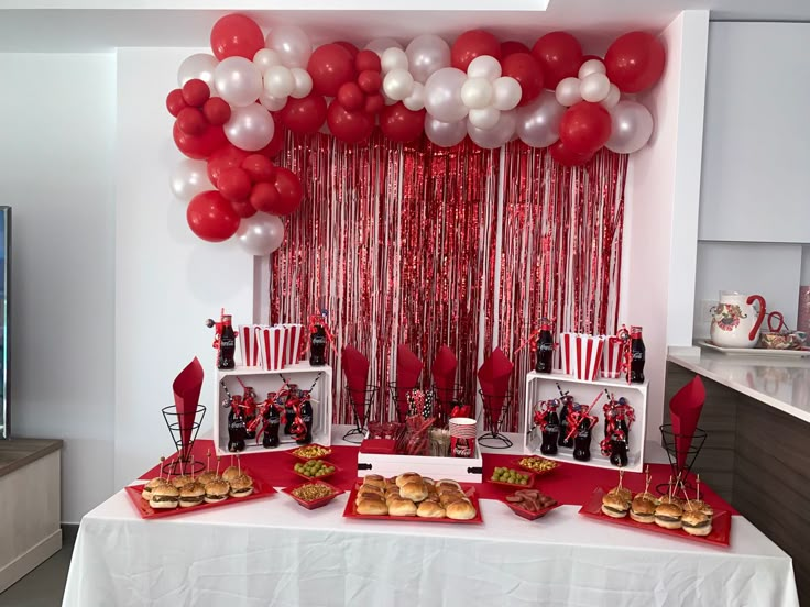 a table topped with red and white desserts next to a wall filled with balloons