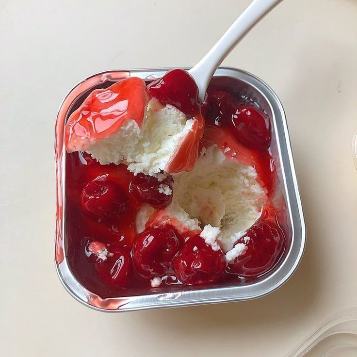 a spoonful of ice cream and cherries in a plastic container on a table