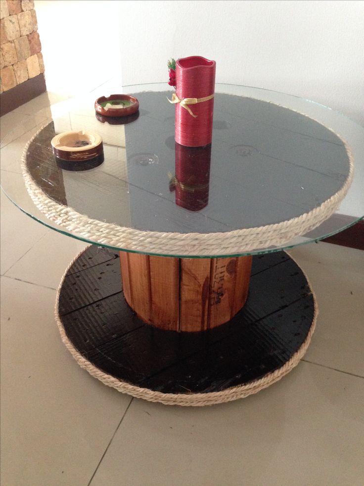 a round glass table with rope around it and a red vase on the bottom shelf