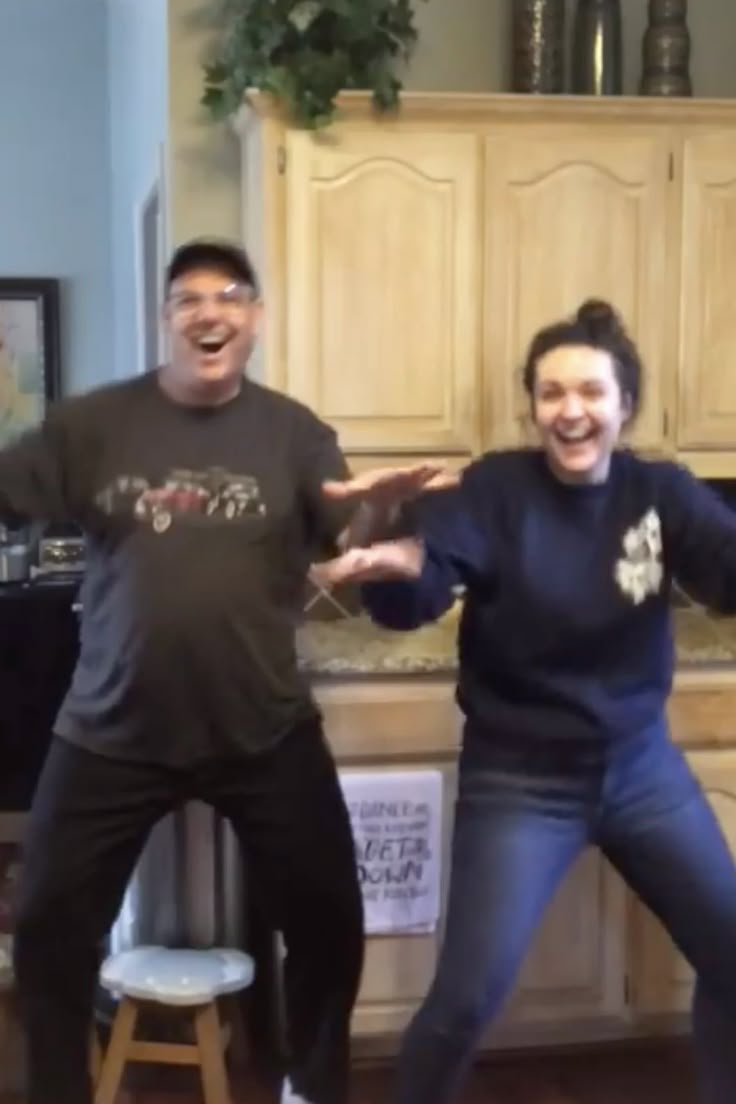 two people standing in front of a kitchen counter with their arms spread out and laughing