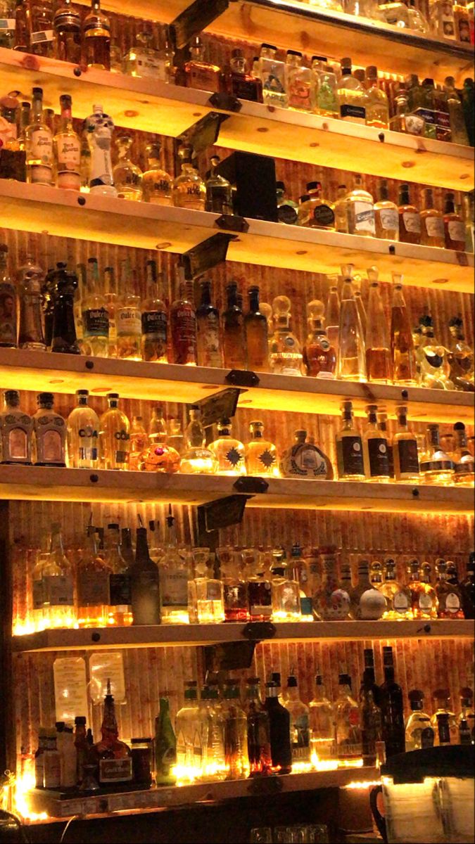 many bottles are on the shelves in a bar with candles lit up behind them and there is no image here to provide a caption