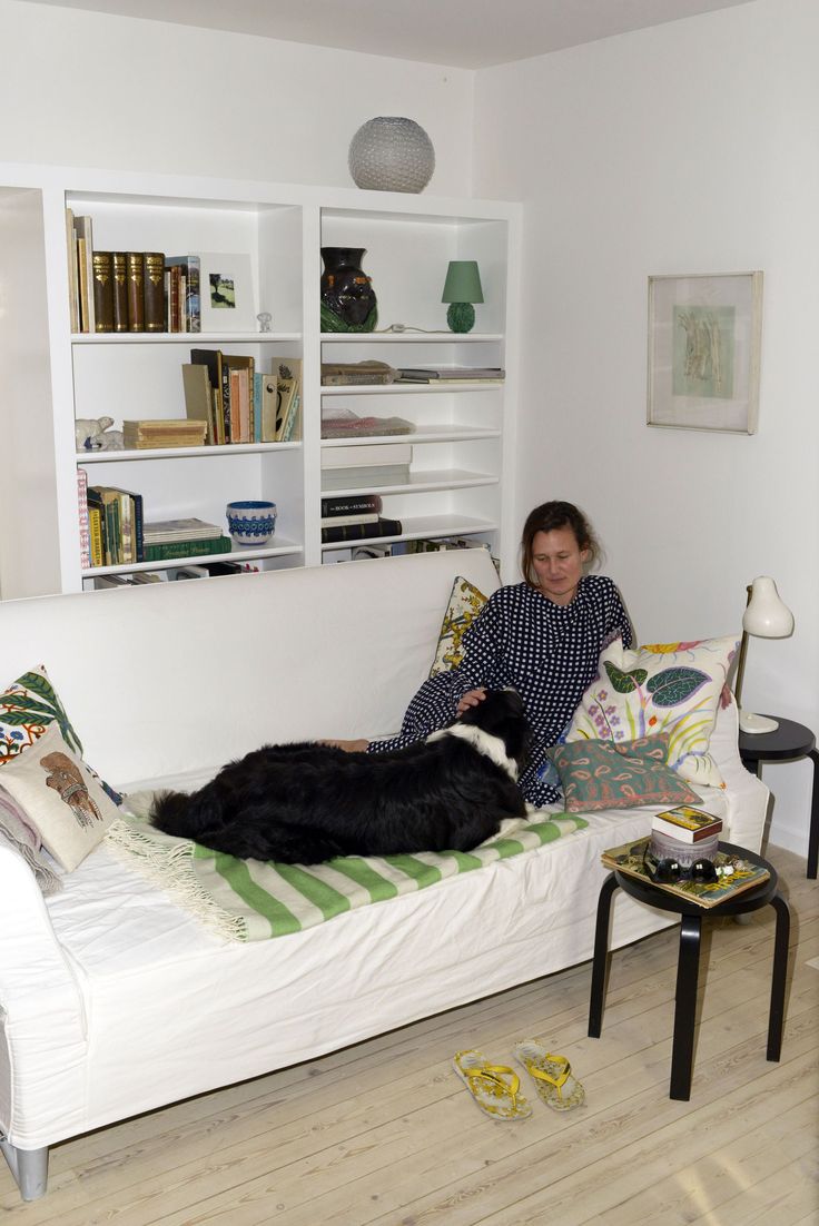 a woman sitting on a white couch with a black dog laying on top of it