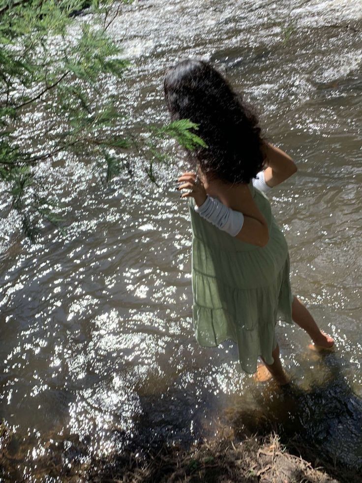 a woman standing in the middle of a river with her back turned to the camera