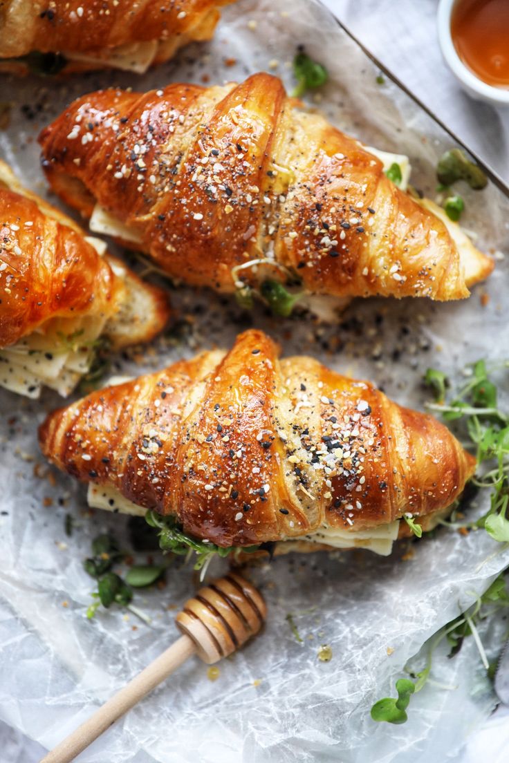 four croissants with sesame seeds and herbs on them, sitting on wax paper