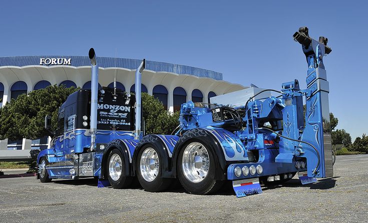 a blue semi truck parked in front of a building with a large circular window on it's side