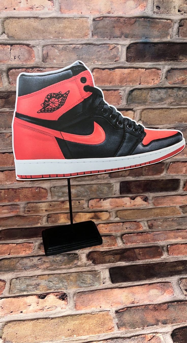 a pair of sneakers is on display in front of a brick wall with a black and red shoe