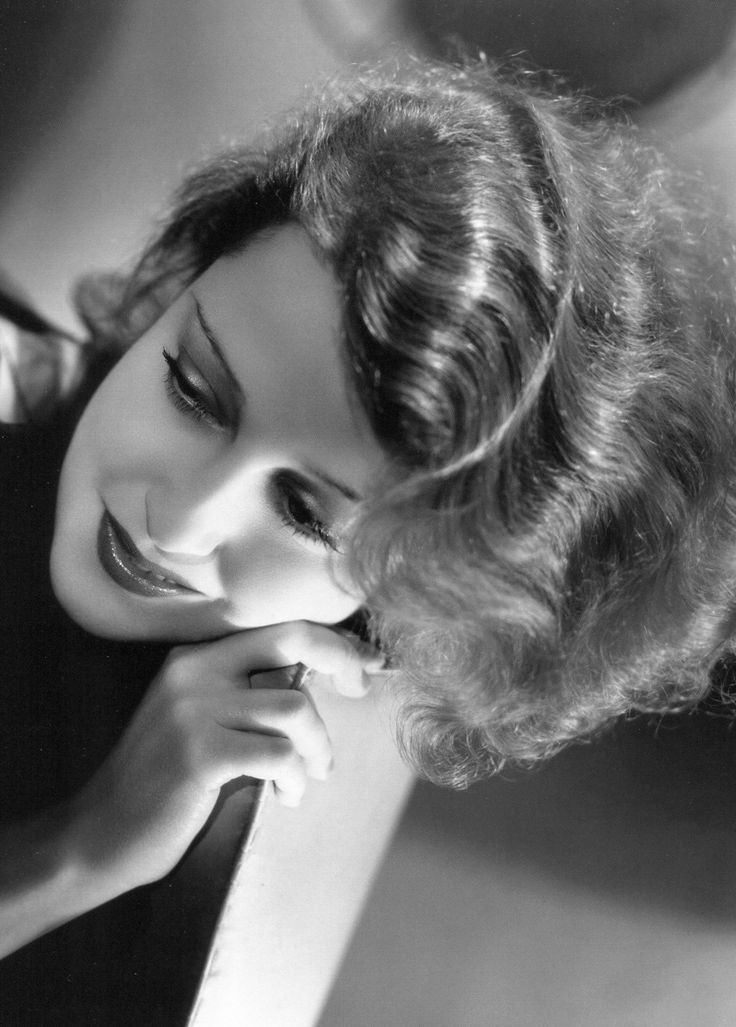 a black and white photo of a woman with her hand on her chin looking at the camera