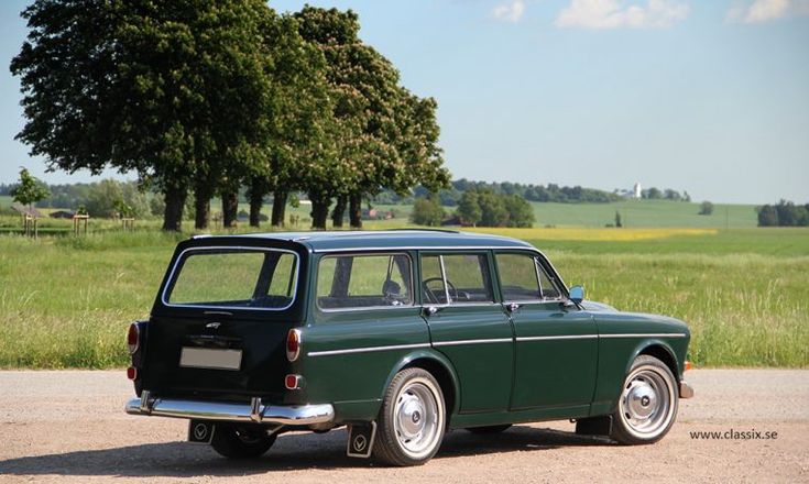 an old green station wagon is parked on the side of the road in front of some trees