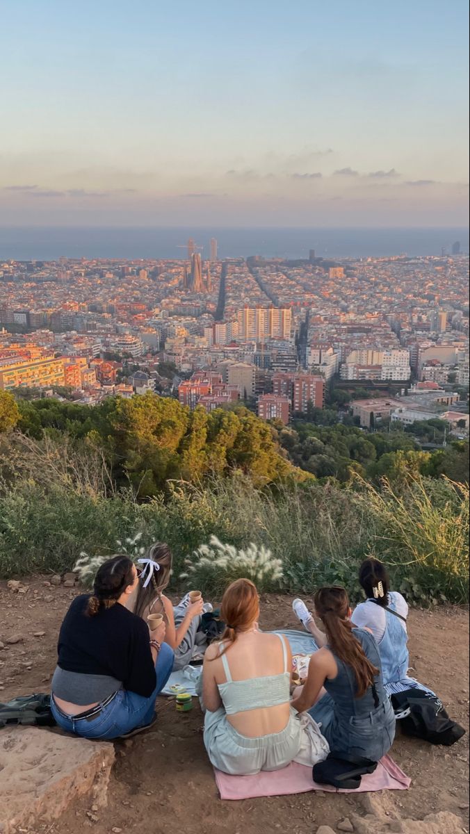 three women sitting on top of a hill overlooking a city