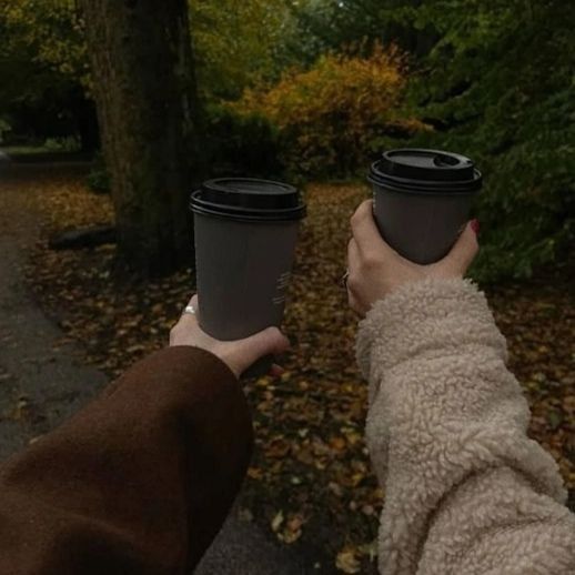 two people are holding coffee cups in their hands while walking through the park on a fall day