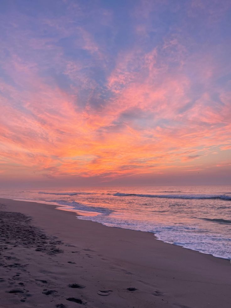 the sun is setting at the beach with footprints in the sand