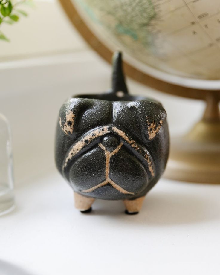 a small black pug figurine sitting on top of a table next to a globe