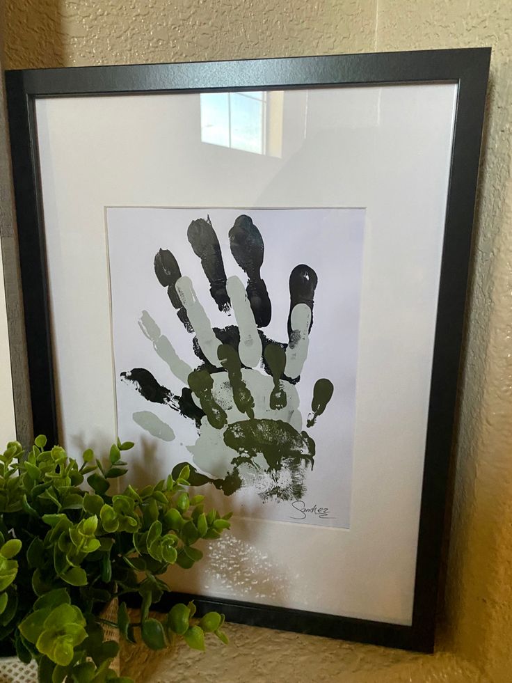 a hand print is displayed on a shelf next to a potted plant and framed photograph