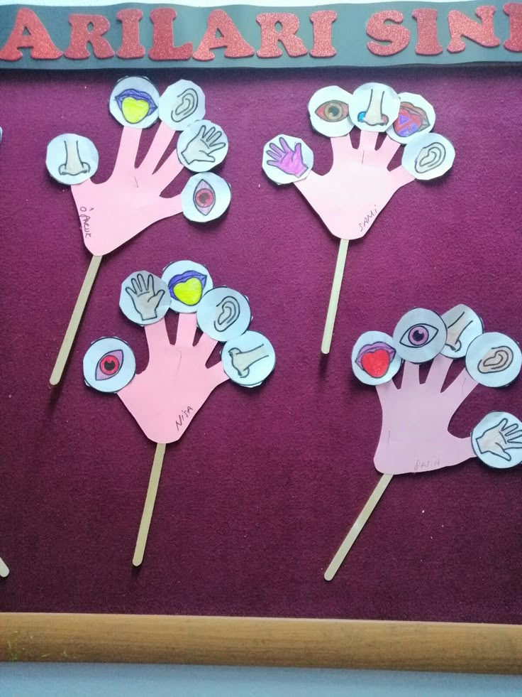 handprinted paper flowers on sticks in front of a bulletin board with words and pictures