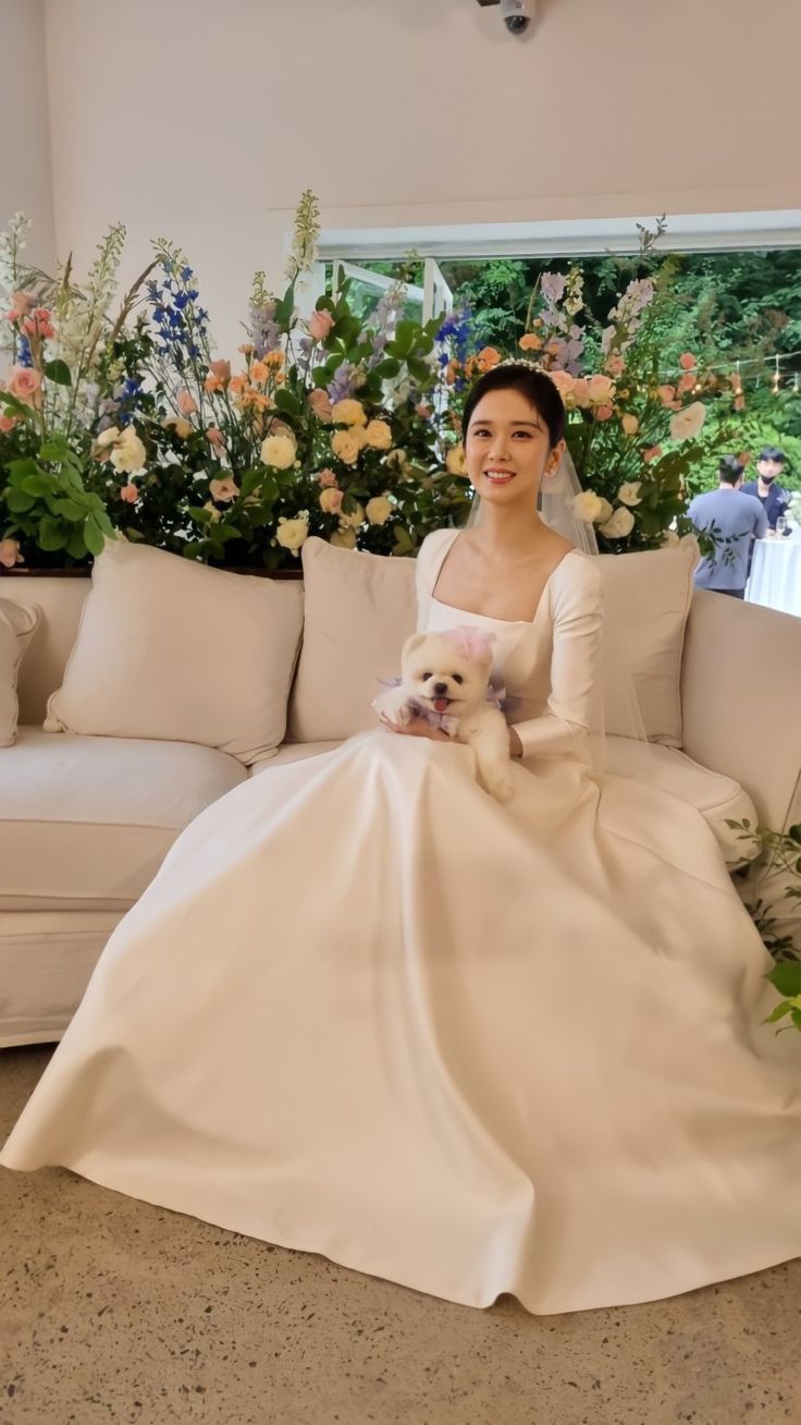 a woman in a white dress sitting on a couch with a dog next to her