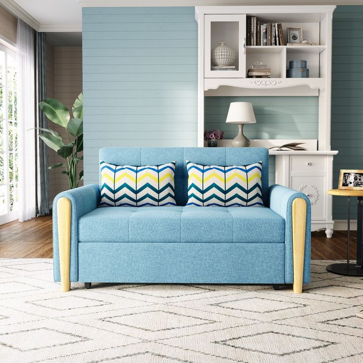 a blue couch with two pillows on it in front of a book shelf and window