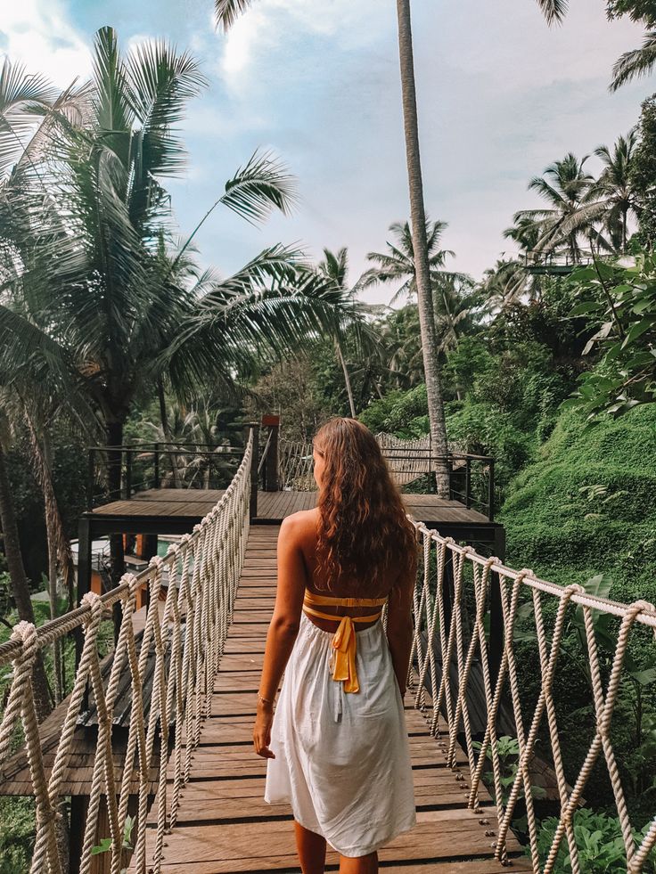 a woman is walking across a rope bridge in the jungle with palm trees behind her