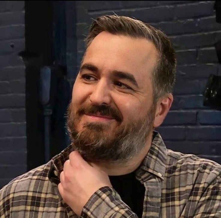 a man with a goatee smiles at the camera while wearing a flannel shirt